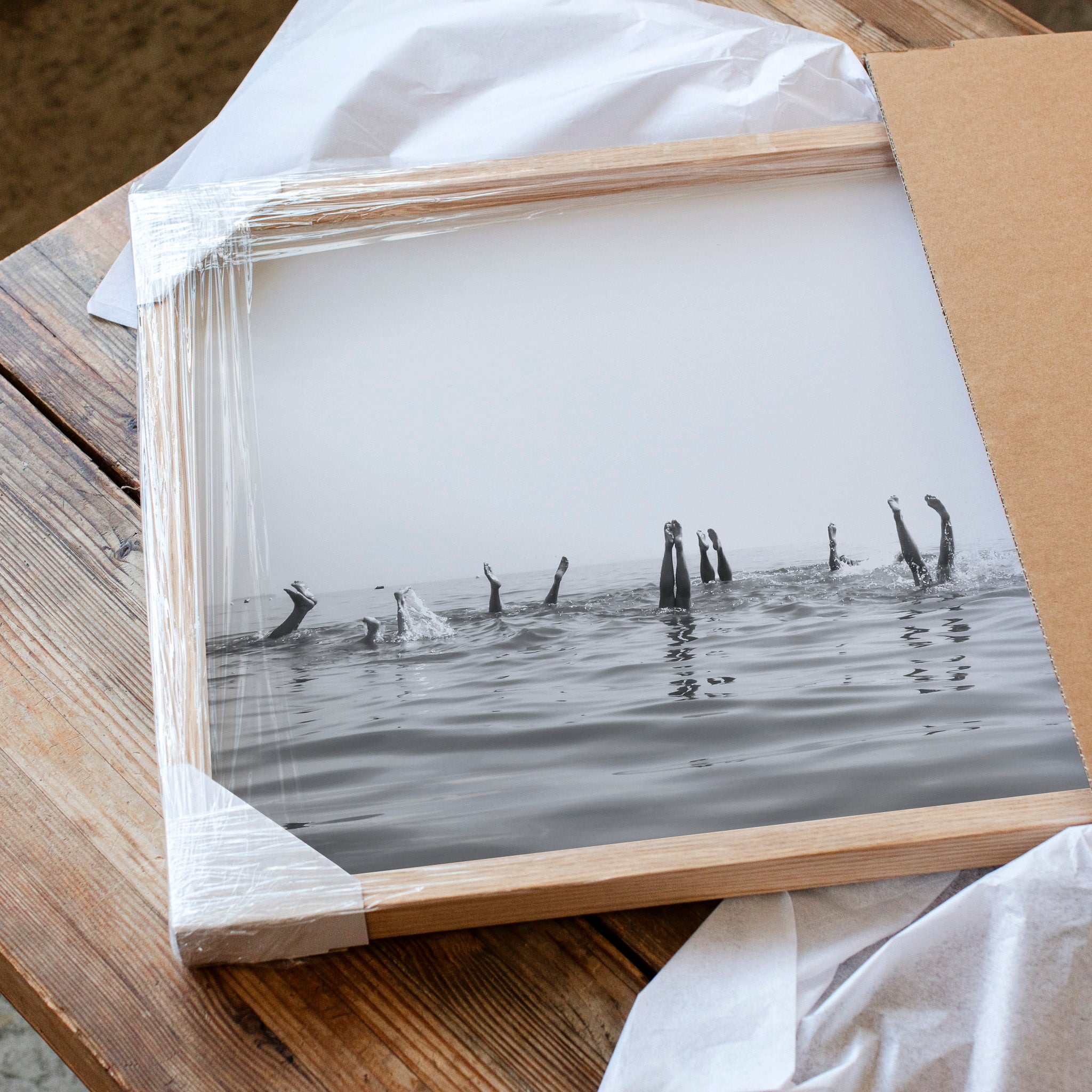 A framed black and white photograph of people swimming in the ocean, with the water appearing calm and the sky above them.