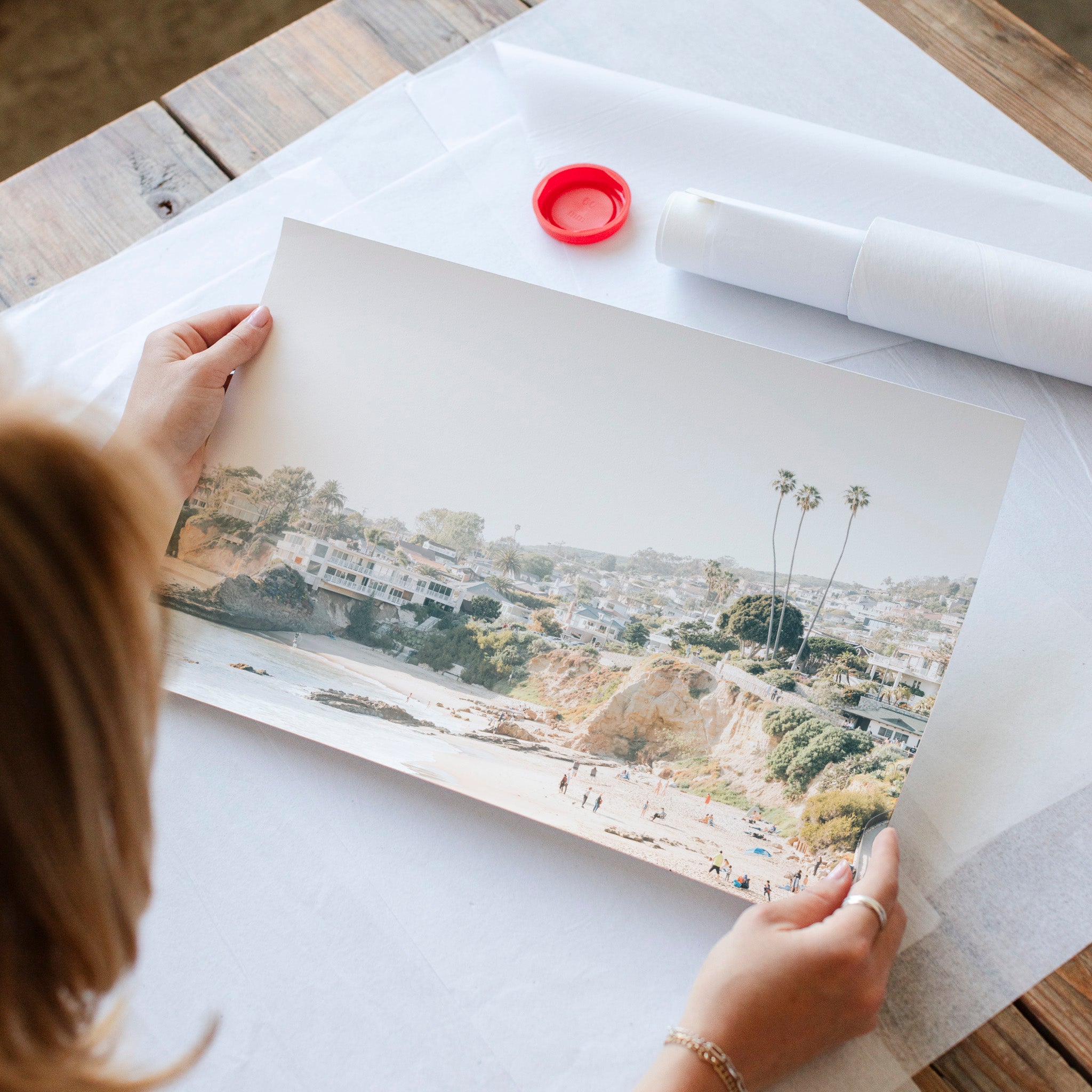 A person is holding a framed photograph of a beach scene, with palm trees and buildings visible in the image.