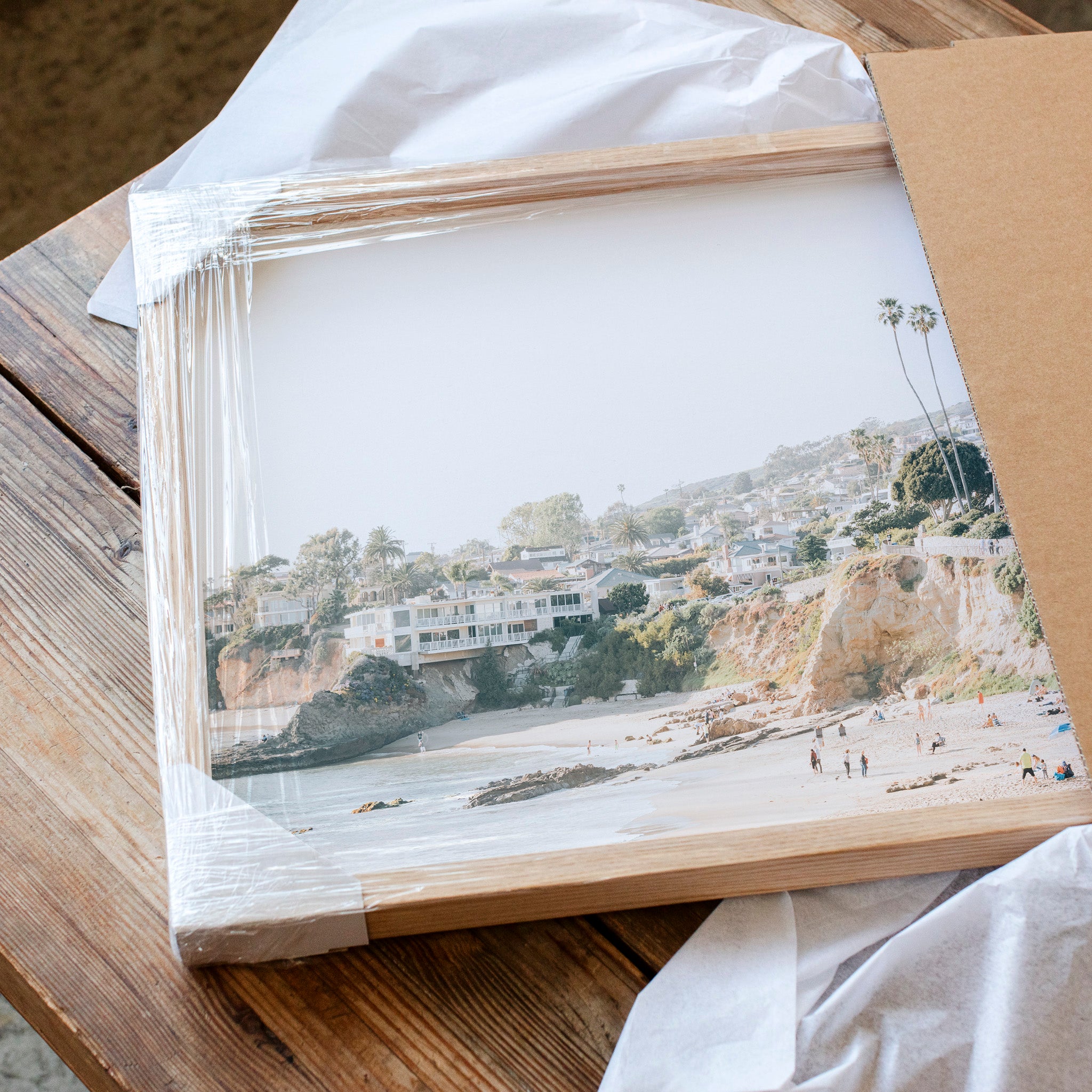 a framed photograph of a beach scene, with a wooden frame and a clear plastic cover. The photograph appears to be a collage of multiple images, and the image is not described in detail.