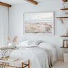 a serene bedroom with a large bed, a framed picture of a beach scene, and a bookshelf filled with books.