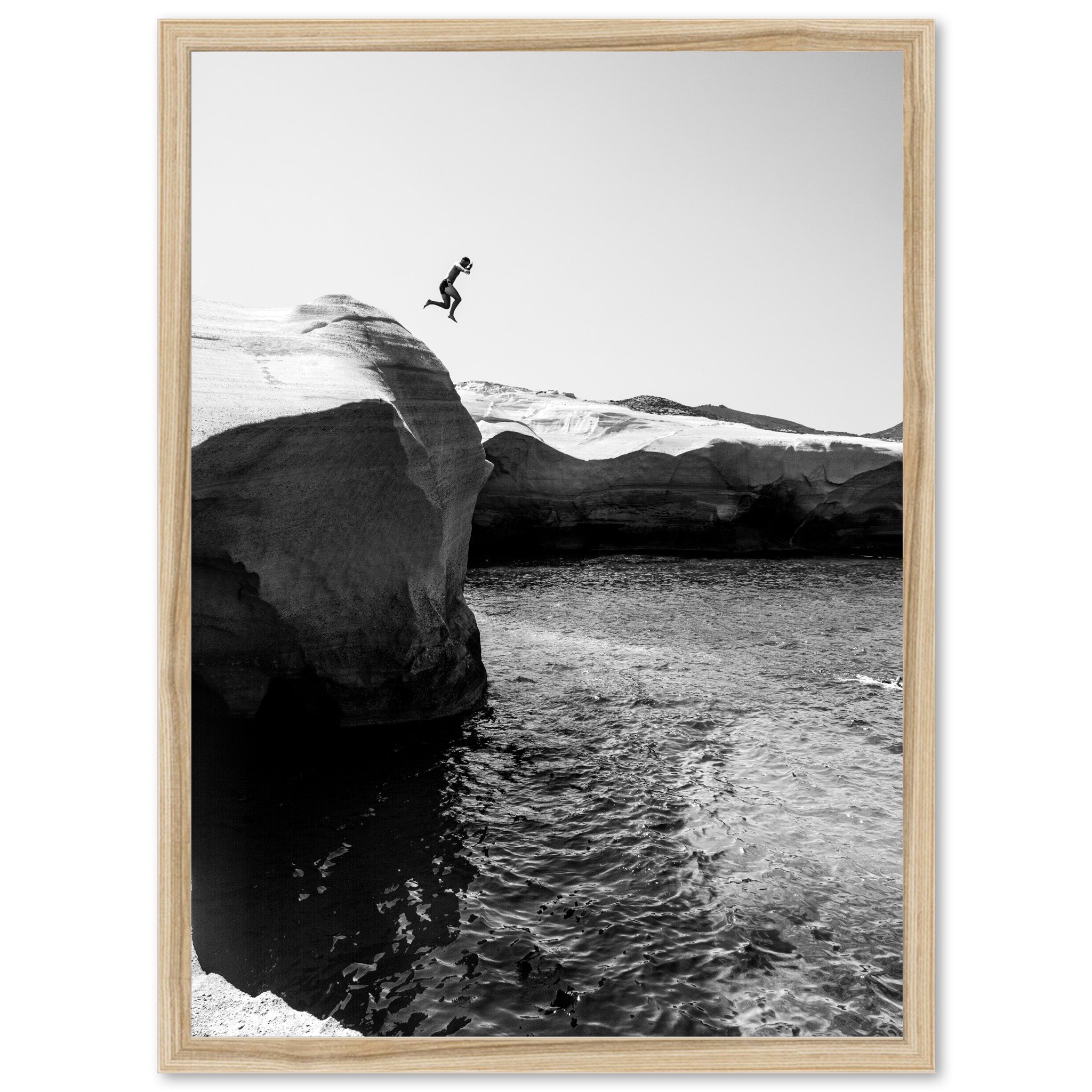 a black and white photo of a person jumping off a cliff into the water