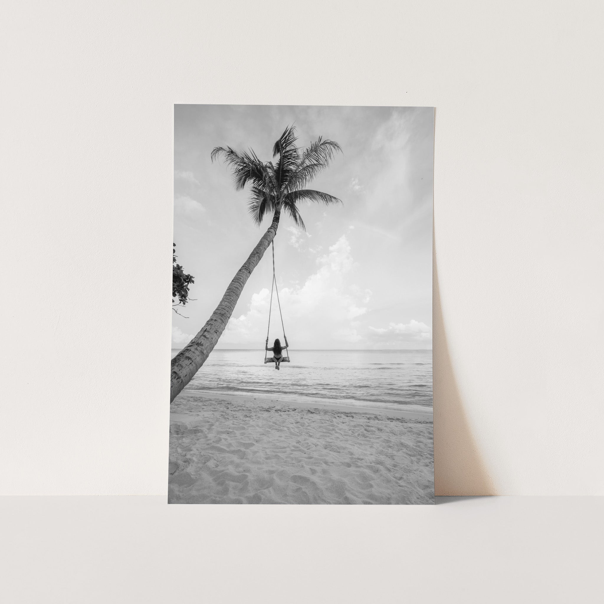 a black and white photo of a person on a swing between two palm trees