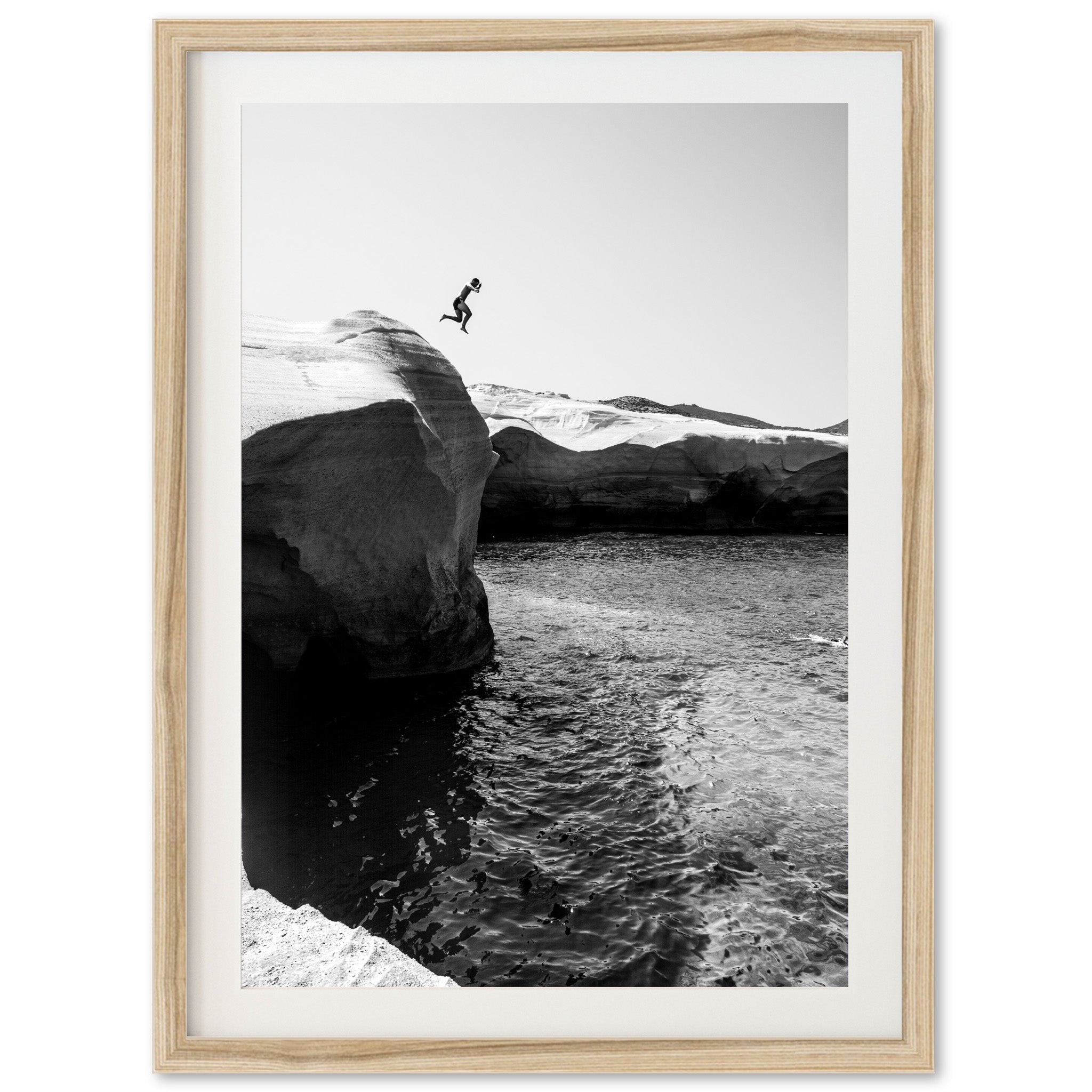 a black and white photo of a person jumping off a cliff into the ocean