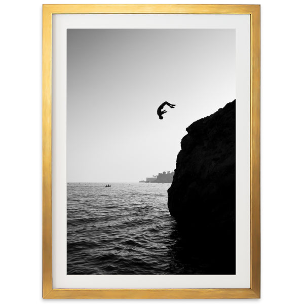 a black and white photo of a person jumping off a cliff into the ocean