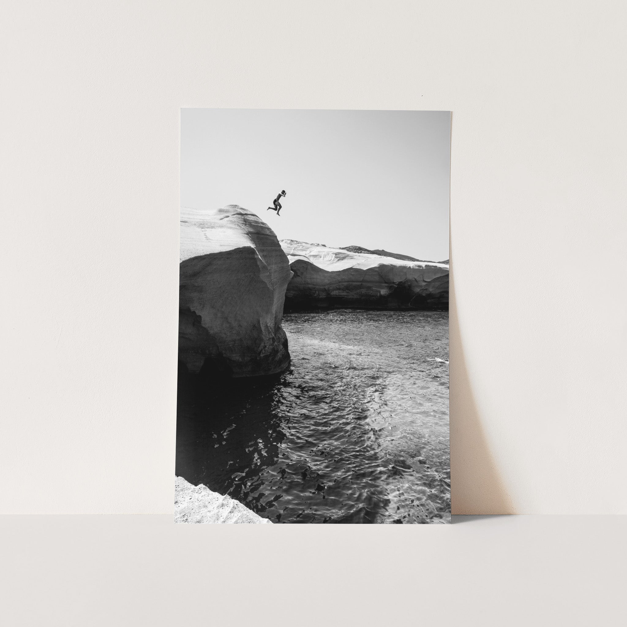 a black and white photo of a person jumping off a cliff into the ocean