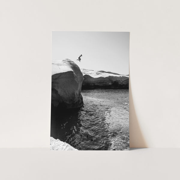 a black and white photo of a person jumping off a cliff into the ocean