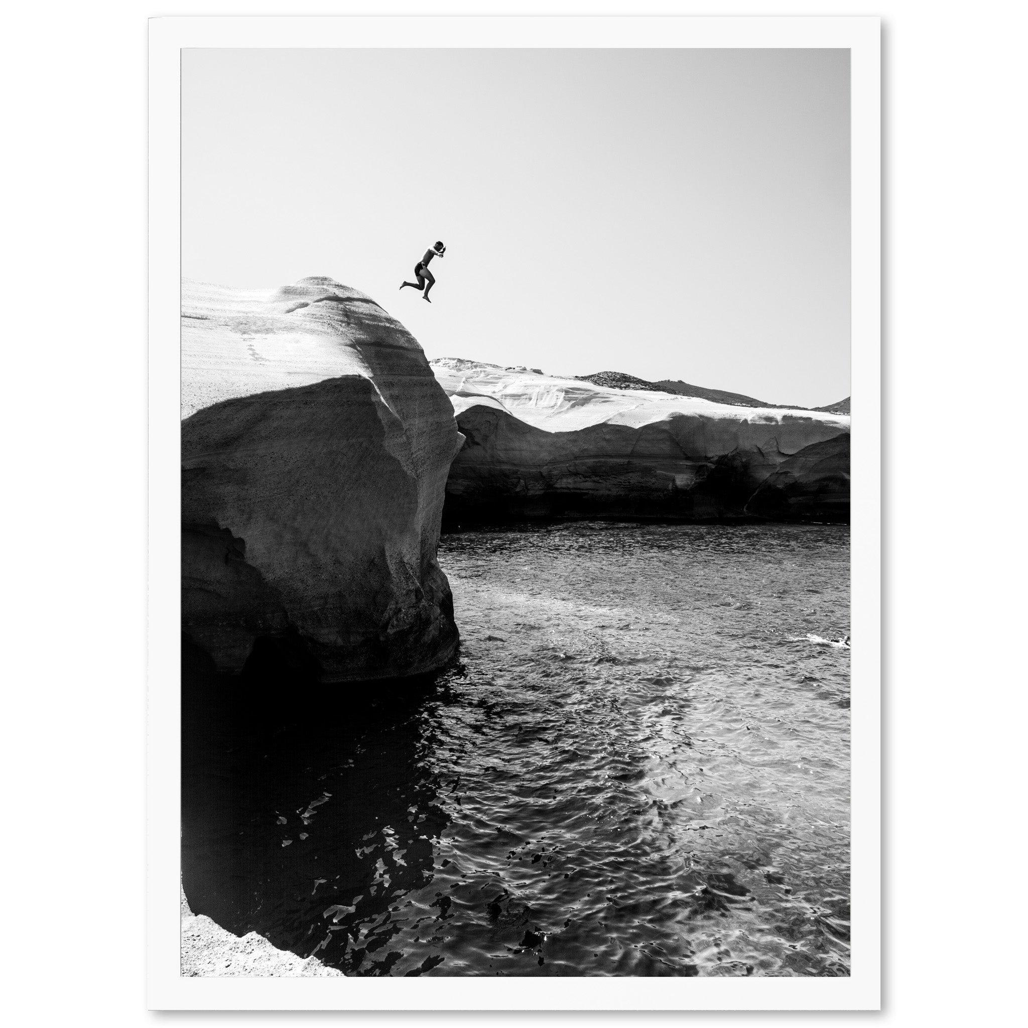 a black and white photo of a person jumping off a cliff into the ocean