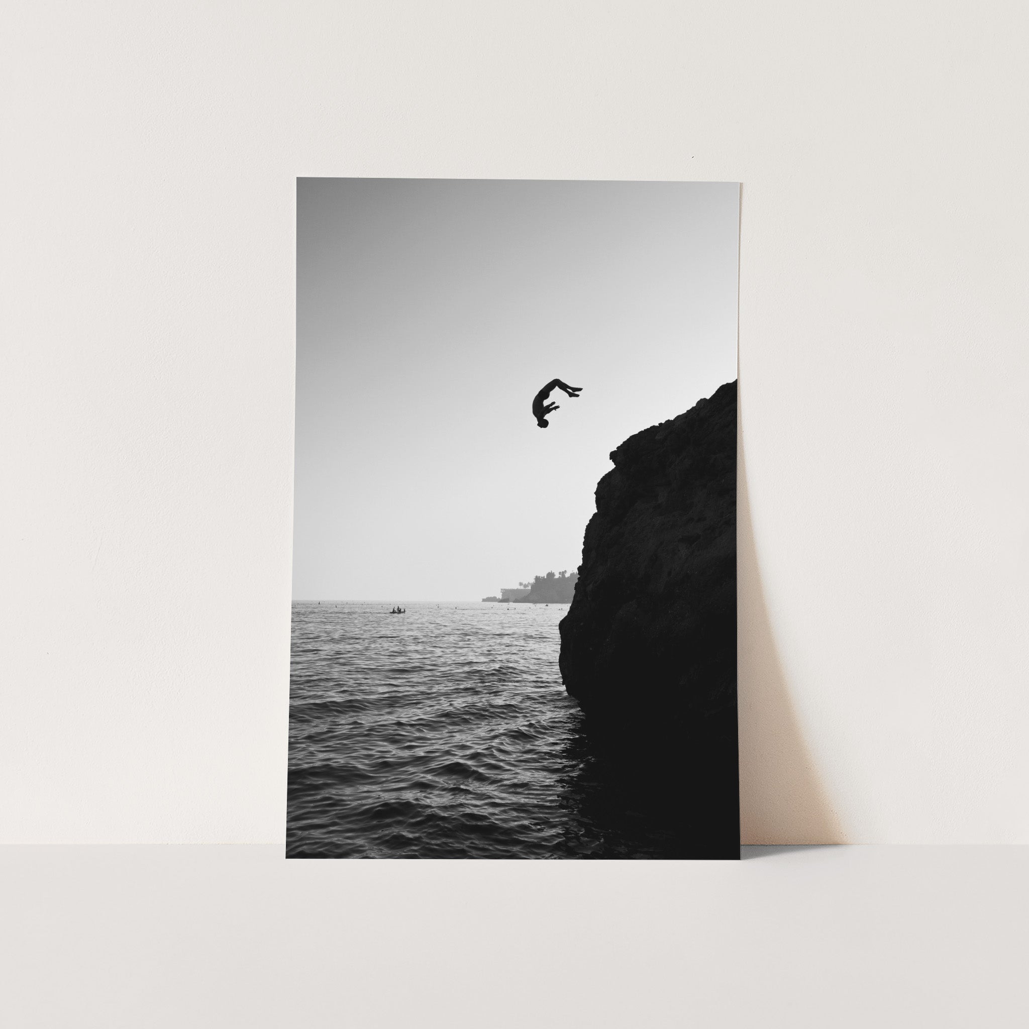 a black and white photo of a person jumping off a cliff into the ocean