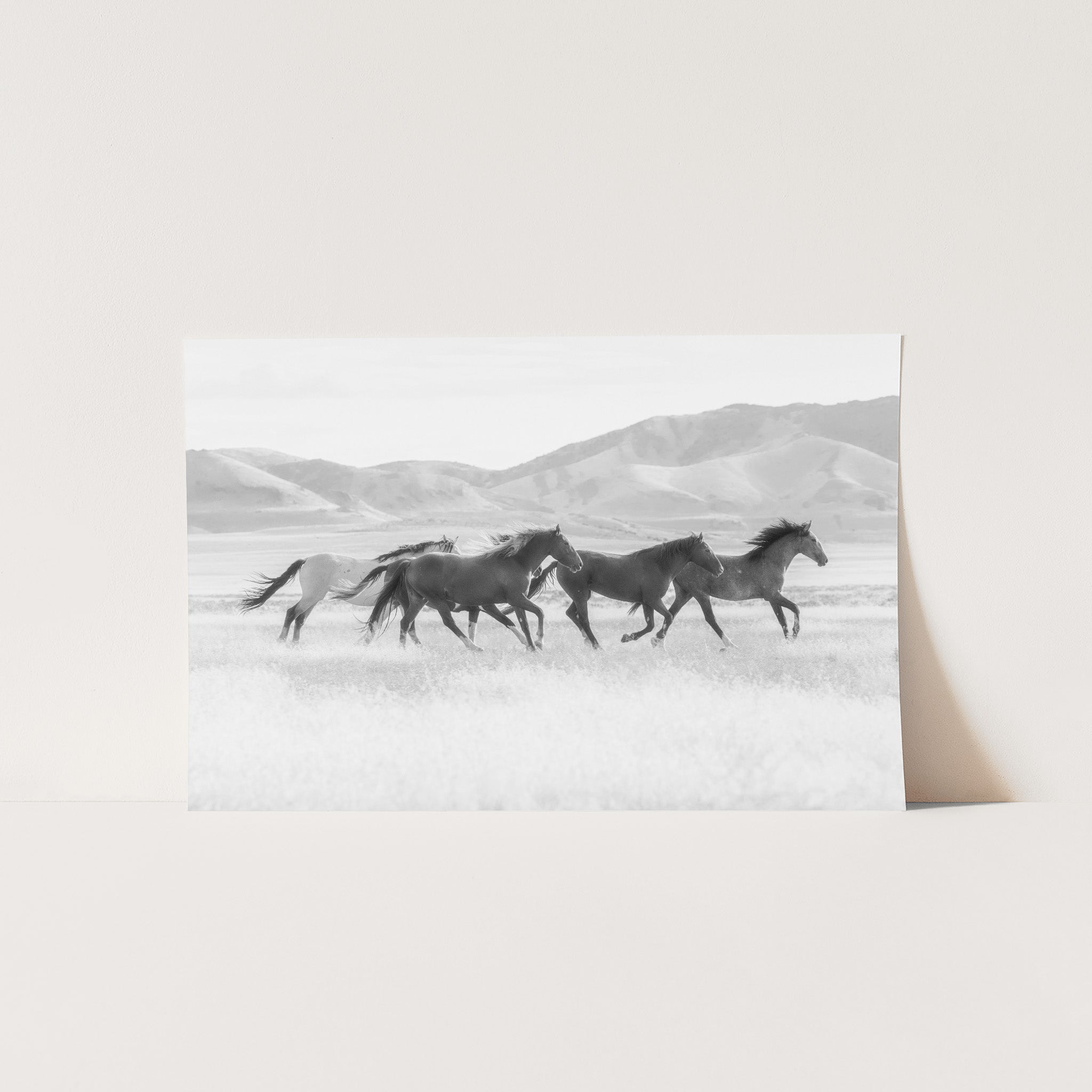 a black and white photo of three horses running in a field