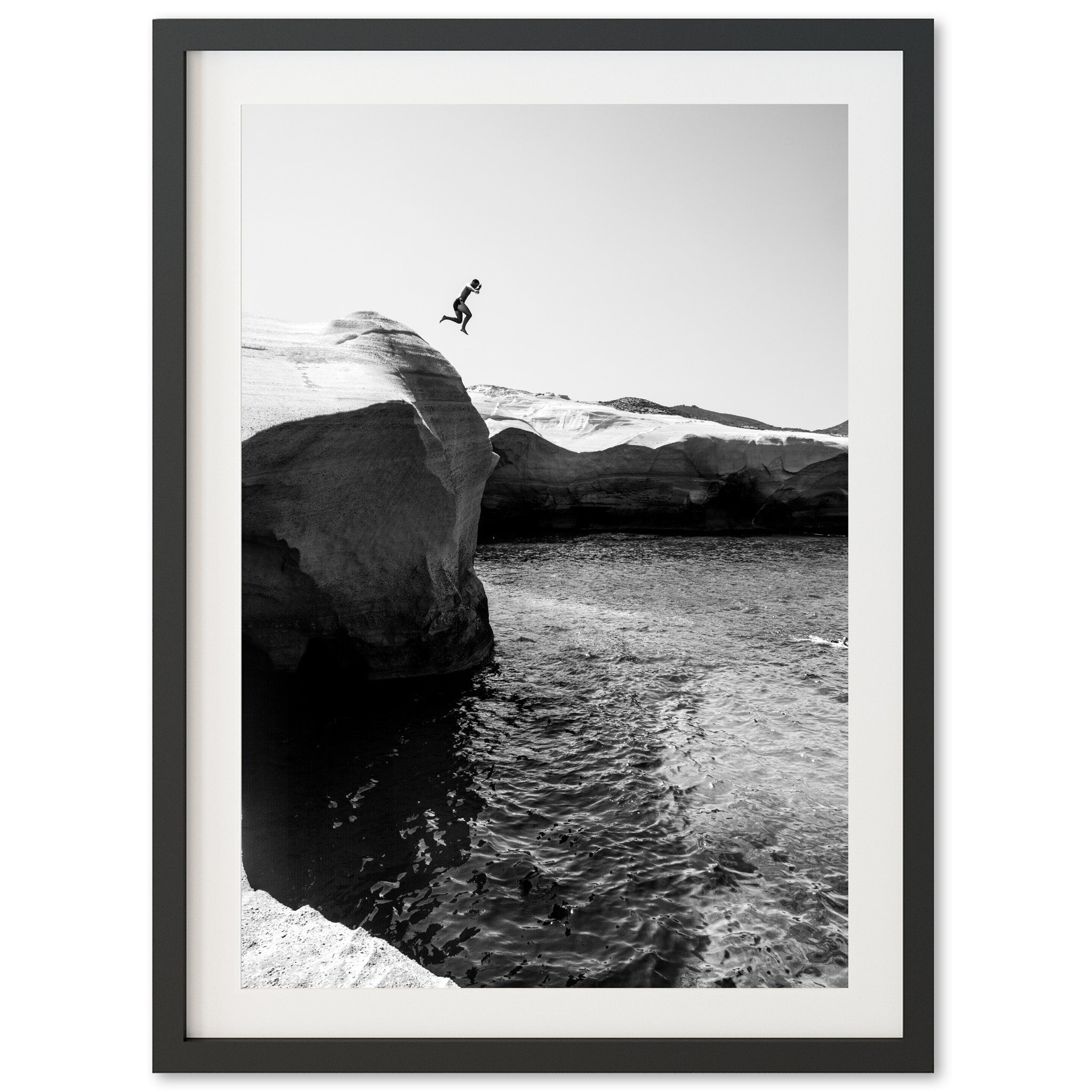 a black and white photo of a person jumping off a cliff into the ocean