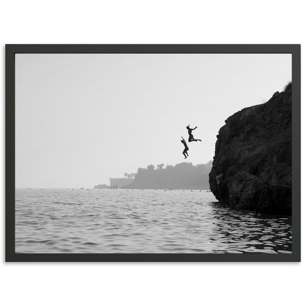 a black and white photo of two people jumping off a cliff into the water