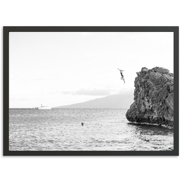 a black and white photo of a person jumping off a cliff into the ocean